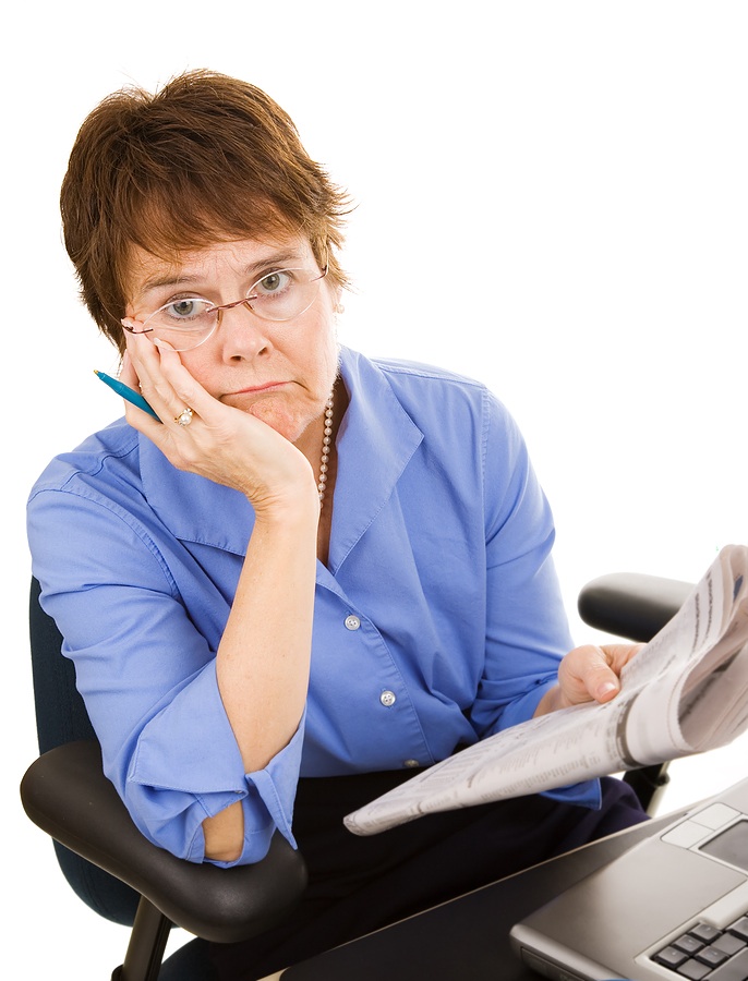 Woman sitting at laptop with newspaper in hand. Not happy. 